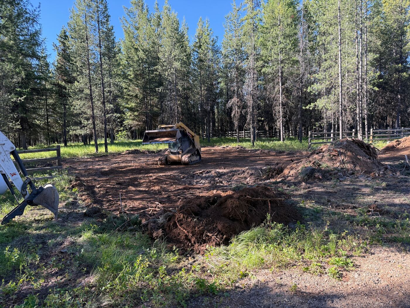 A track loader working cleared ground with stumps and root wads piled to one side