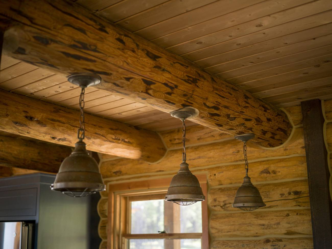 Exposed log ridge beam and pendant lights against a boarded ceiling