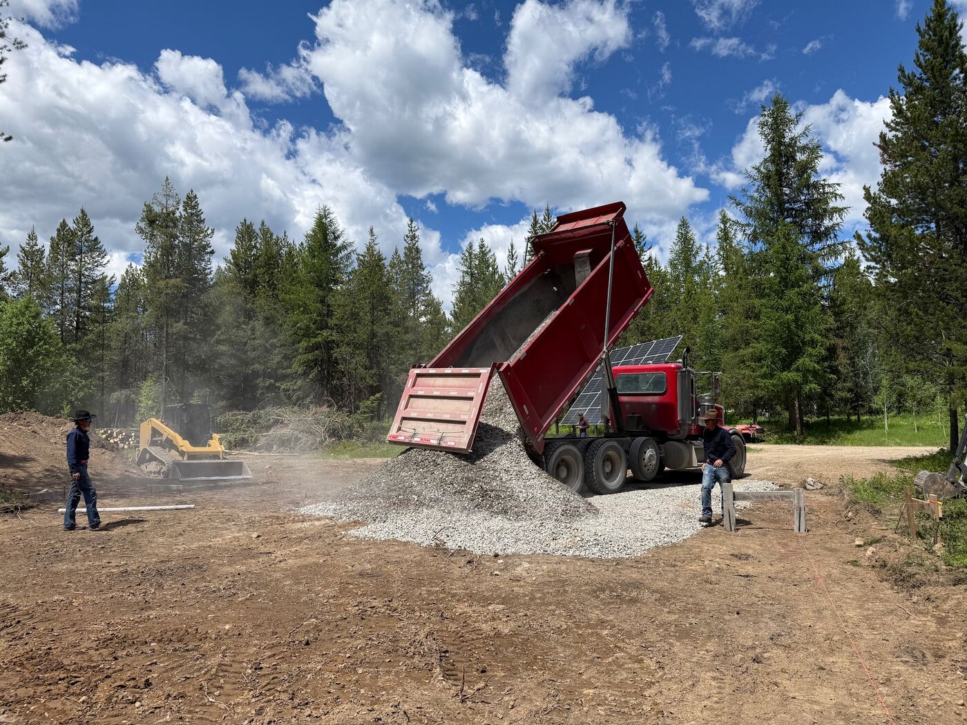 A dump truck placing crushed base while an excavator spreads it